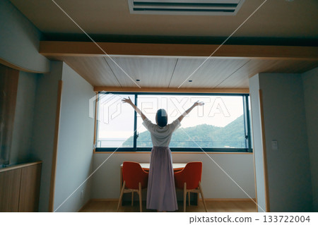 一位二十多歲的女子正從飯店房間欣賞壯麗的景色。 133722004