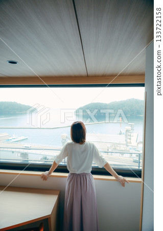 A scene of a woman in her twenties looking at the view from a hotel window A scene of a woman in her twenties looking at the view from a hotel window 133722158