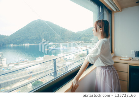 A scene of a woman in her twenties looking at the view from a hotel window A scene of a woman in her twenties looking at the view from a hotel window 133722166