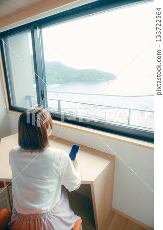 一位二十多歲的女性在飯店房間裡看著她的智慧型手機。 133722564