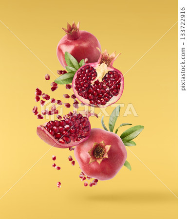 Flying in air fresh ripe whole and cut pomegranate with seeds and leaves isolated. High resolution image 133722916