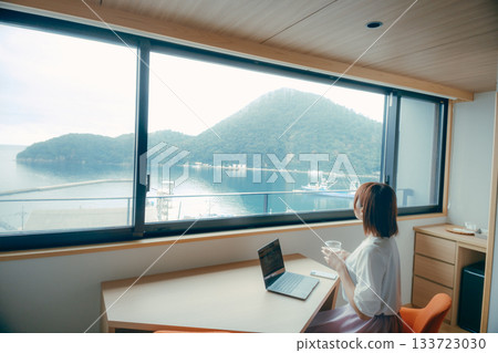 A scene of a woman in her twenties working on a computer in a hotel room 133723030