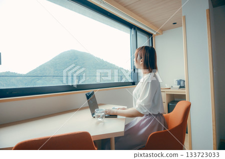 A scene of a woman in her twenties working on a computer in a hotel room 133723033