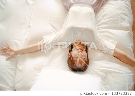 一位二十多歲的女子在飯店白色床上放鬆休息的場景 133723352