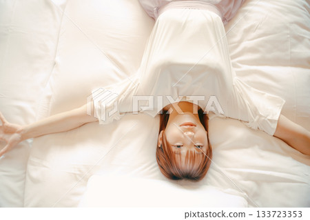一位二十多歲的女子在飯店白色床上放鬆休息的場景 133723353