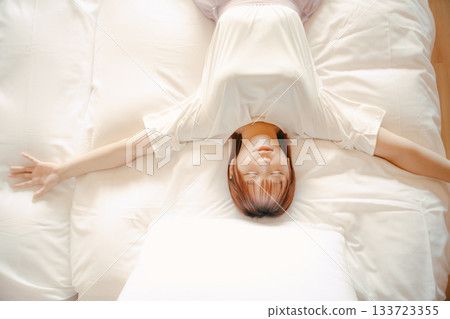 一位二十多歲的女子在飯店白色床上放鬆休息的場景 133723355