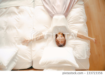A scene of a woman in her twenties relaxing on a white bed in a hotel 133723356