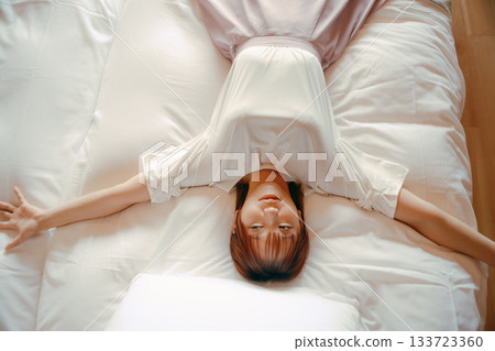 A scene of a woman in her twenties relaxing on a white bed in a hotel A scene of a woman in her twenties relaxing on a white bed in a hotel 133723360