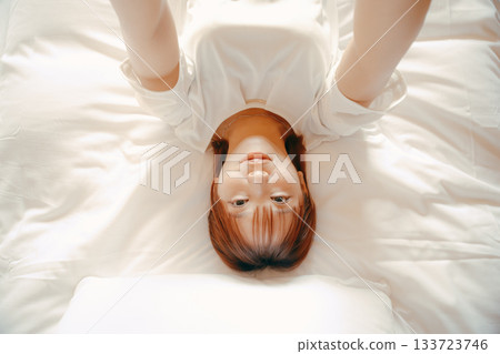 一位二十多歲的女子在飯店床上用智慧型手機自拍的場景 133723746