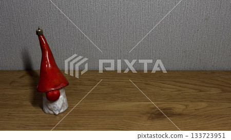 Charming Red-Hatted Gnome Figurine on Wooden Surface Charming Red-Hatted Gnome Figurine on Wooden Surface 133723951