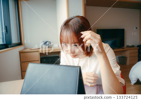 A woman in her 20s looking in the mirror in a hotel room and adjusting her appearance | Travel, accommodation, makeup 133724125