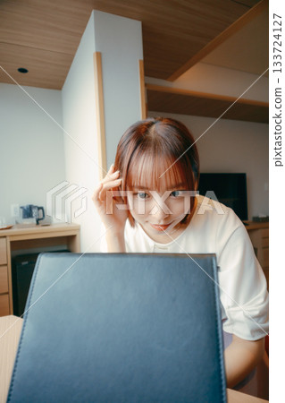 A woman in her 20s looking in the mirror in a hotel room and adjusting her appearance | Travel, accommodation, makeup 133724127