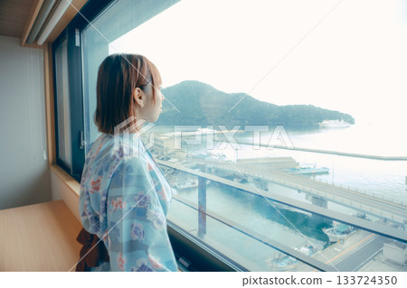 A scene of a woman in her 20s in a yukata robes looking out the window at the sea 133724350