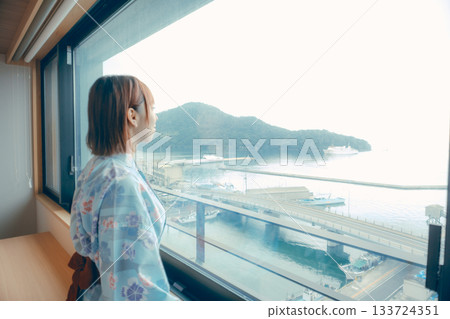 A scene of a woman in her 20s in a yukata robes looking out the window at the sea 133724351