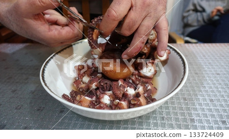 Cutting freshly boiled octopus with scissors to prepare it for the salad. Cutting freshly boiled octopus with scissors to prepare it for the salad. 133724409
