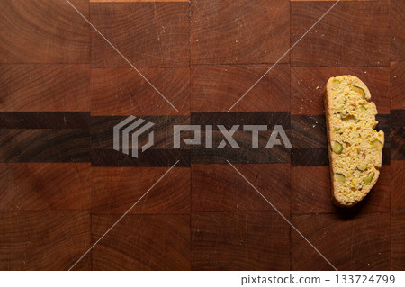 Single, homemade, orange and pistachio holiday biscotti on a wooden cutting board 133724799