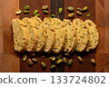 Pistachio biscotti cookies surrounded by pistachios on a wood cutting board 133724802