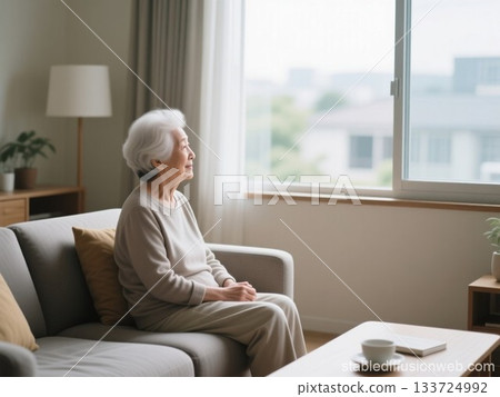 一位頭髮花白的老婦人坐在明亮的房間沙發上,望著窗外。 一位頭髮花白的老婦人坐在明亮的房間沙發上,望著窗外。 133724992