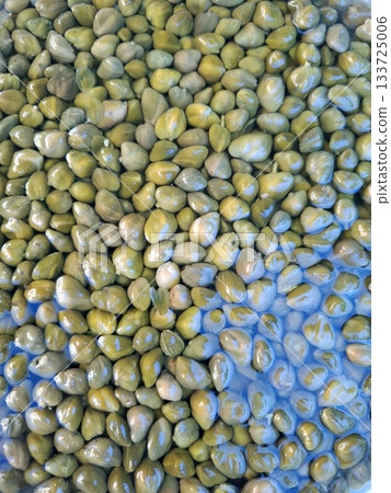 Rows of salted capers rest in a basin, showcasing their bright green and varied tones. The texture and color reflect their readiness for diverse culinary applications. 133725006