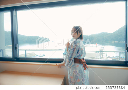一位二十多歲的女子身穿浴衣,正從飯店窗戶向外眺望風景。 一位二十多歲的女子身穿浴衣,正從飯店窗戶向外眺望風景。 133725884