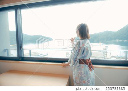 一位二十多歲的女子身穿浴衣，正從飯店窗戶向外眺望風景。 133725885
