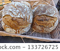 Homemade bread sits invitingly in a basket at a vibrant farmers' market in Spain. Local vendors showcase their goods on a warm afternoon, attracting eager customers. 133726725