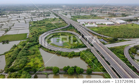 Aerial drone shot of a highway interchange overpass amidst lush green rice paddies and a river, showcasing infrastructure in nature. 133726961