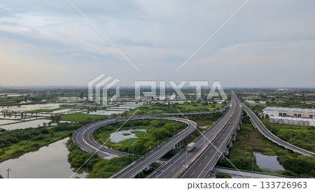 Aerial drone shot of a highway interchange overpass amidst lush green rice paddies and a river, showcasing infrastructure in nature. 133726963