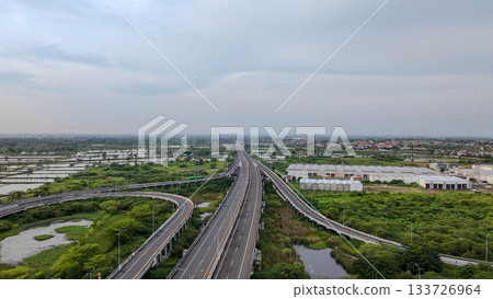 Aerial drone shot of a highway interchange overpass amidst lush green rice paddies and a river, showcasing infrastructure in nature. 133726964