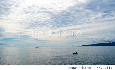 The ocean and the silhouette of a fishing boat under a cloudy sky 133727114