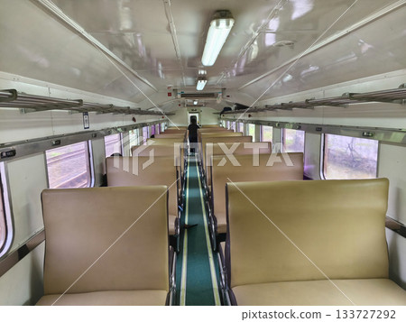Interior of an empty Indonesian train carriage, featuring rows of beige seats and overhead luggage racks. The aisle is visible to the back. Interior of an empty Indonesian train carriage, featuring rows of beige seats and overhead luggage racks. The aisle is visible to the back. 133727292