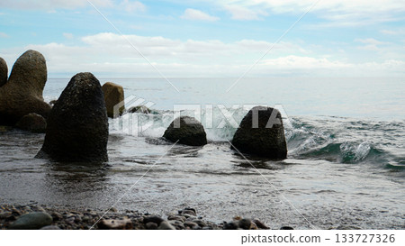 Waves crashing against wave-dissipating blocks buried in the sand Waves crashing against wave-dissipating blocks buried in the sand 133727326