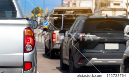 Rear side of pickup car silver color stop on the road by traffic light control. Several cars were parked next to the traffic light. Blurred background of town and blue sky. 133728764