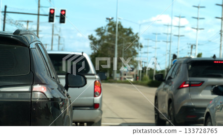 Rear side of black car with turn on brake light. Stop on concrete road by traffic red light control. Many car stop in junction road. Background of electric pole and trees at day in Thailand. 133728765