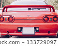 A bright red sports car, seen from the rear, with a large rear spoiler and round taillights. A stylish retro feel and a strong emphasis on the car's design. Car racing, street racing. 133729097