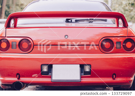 A bright red sports car, seen from the rear, with a large rear spoiler and round taillights. A stylish retro feel and a strong emphasis on the car's design. Car racing, street racing. 133729097