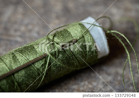 Green embroidery thread is placed next to a needle Green embroidery thread is placed next to a needle 133729148