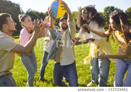 Happy joyful young people friends having fun in summer park playing with ball. Happy joyful young people friends having fun in summer park playing with ball. 133729491
