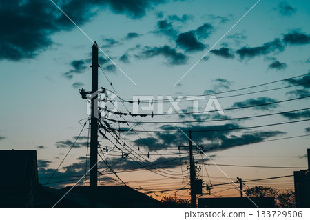 Silhouettes of electric poles and power lines and clouds floating in the twilight sky Silhouettes of electric poles and power lines and clouds floating in the twilight sky 133729506