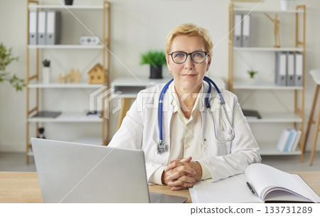 Mature female doctor smiling at desk, medical consultant, female medical nurse or practitioner 133731289