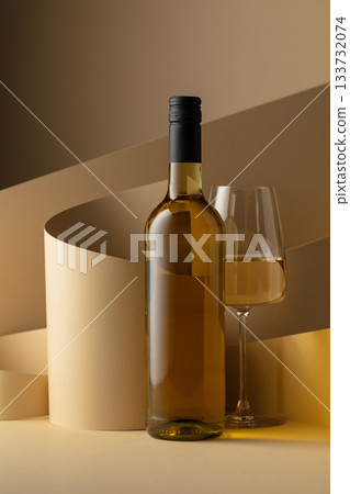 Bottle and glass of white wine on a beige background. Bottle and glass of white wine on a beige background. 133732074
