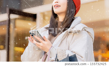 一位女士在白雪皚皚的冬日街角使用智慧型手機。 133732425
