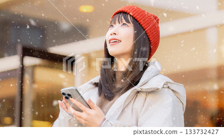 A woman using a smartphone on a snowy winter street corner 133732427
