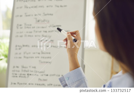Young business woman standing in front of planner whiteboard planning the tasks on a week. Young business woman standing in front of planner whiteboard planning the tasks on a week. 133732517