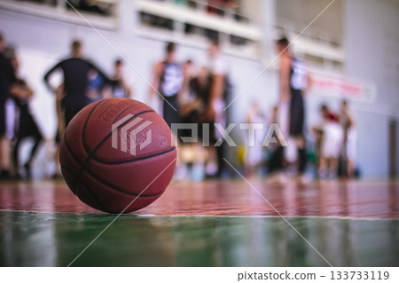 A detailed close-up of a basketball on the court. The blurred stands create a dynamic background, making it ideal for ads, magazine covers, and promoting a healthy lifestyle. Features copy space. A detailed close-up of a basketball on the court. The blurred stands create a dynamic background, making it ideal for ads, magazine covers, and promoting a healthy lifestyle. Features copy space. 133733119