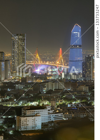 A stunning nightscape of Bangkok's business district, showcasing illuminated skyscrapers and the majestic Bhumibol Bridge glowing brightly after sunset. 133733247