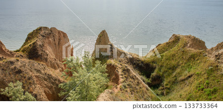 A panoramic view of steep clay cliffs covered with grass and shrubs, descending to the sparkling waters of the Dnieper-Bug Estuary in the Kherson region, Ukraine. A panoramic view of steep clay cliffs covered with grass and shrubs, descending to the sparkling waters of the Dnieper-Bug Estuary in the Kherson region, Ukraine. 133733364