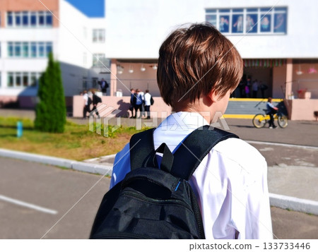 Schoolboy Walking to School with Backpack. Rear view of young boy in white shirt and black backpack heading toward school building on sunny morning. Back to school concept. Schoolboy Walking to School with Backpack. Rear view of young boy in white shirt and black backpack heading toward school building on sunny morning. Back to school concept. 133733446