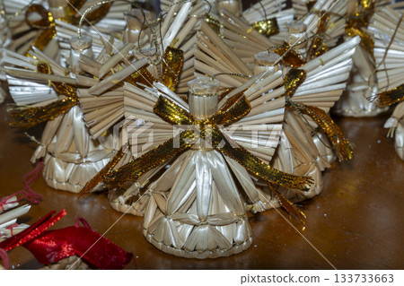 Close-up of numerous small angel-shaped souvenirs woven from straw. 133733663