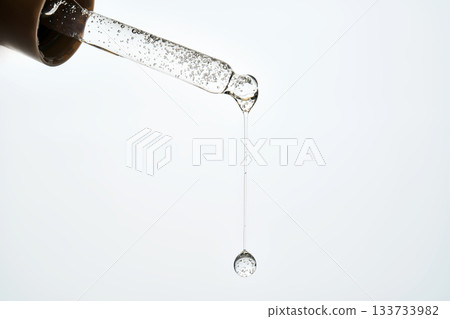 Cosmetic pipette dispensing serum drop against white background Cosmetic pipette dispensing serum drop against white background 133733982